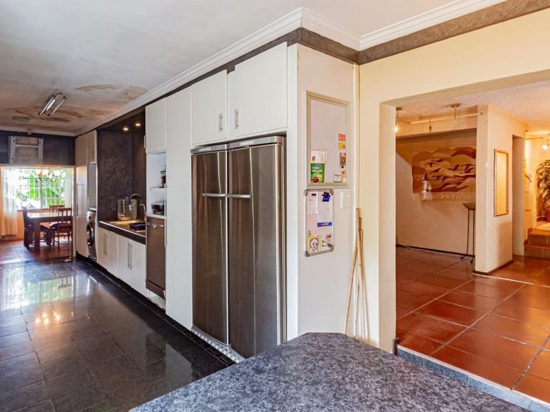 A functional kitchen featuring built-in cabinetry, stainless steel appliances, and stone countertops, adjacent to a tiled living area with visible ceiling maintenance requirements.
