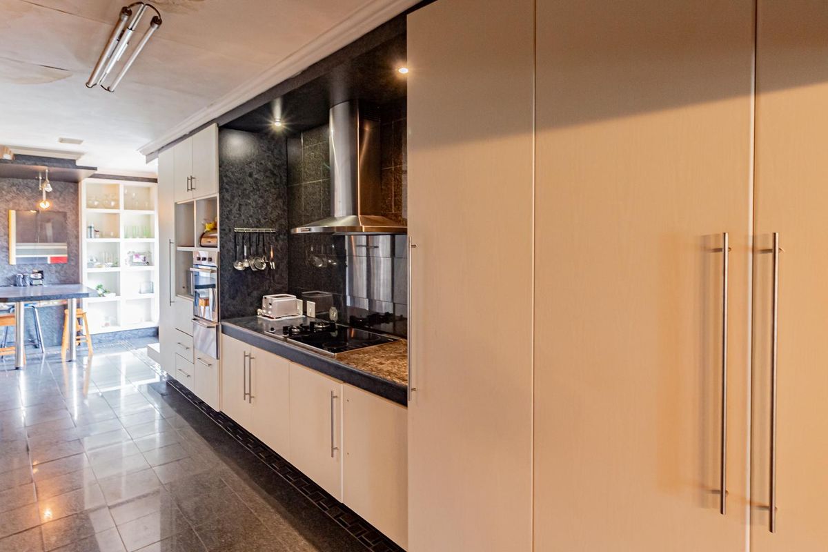 A modern kitchen featuring sleek cabinetry, stone countertops, integrated appliances, and tiled flooring, with an adjacent dining area and built-in shelving.