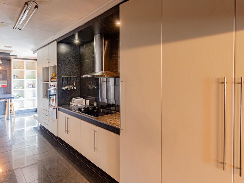A modern kitchen featuring sleek cabinetry, stone countertops, integrated appliances, and tiled flooring, with an adjacent dining area and built-in shelving.