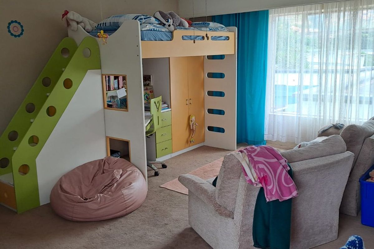 A spacious bedroom featuring a large window with natural light, a ceiling fan, and neutral carpet flooring.