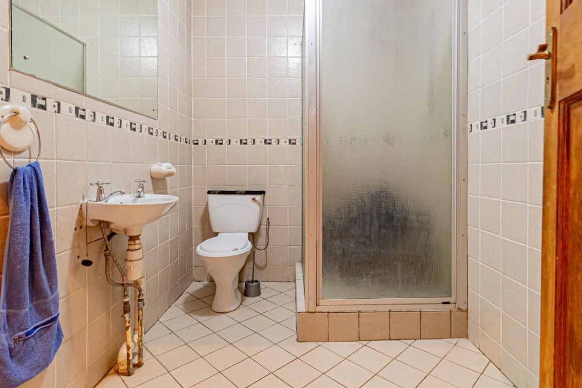 A functional bathroom featuring a shower enclosure, pedestal basin, and toilet, finished with neutral wall and floor tiles.