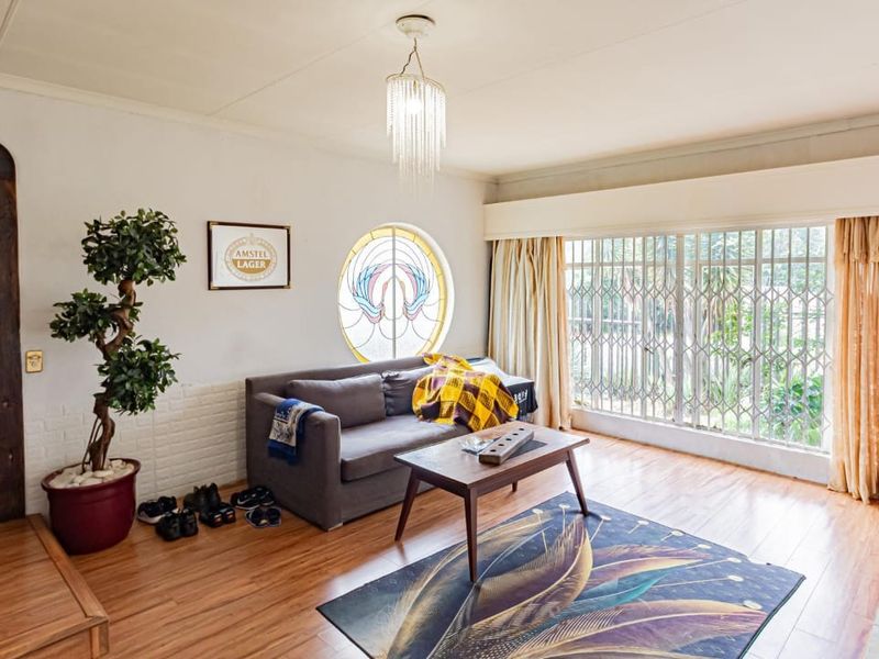 A living room featuring laminate flooring, a unique circular stained glass window, and a large security-gated window overlooking the exterior.