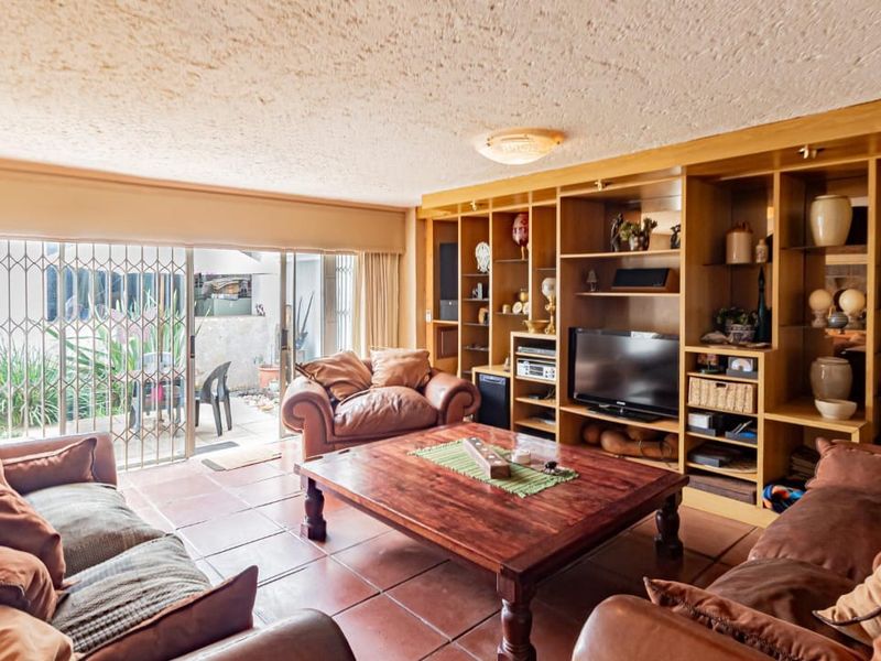 Spacious living room featuring terracotta floor tiles, a large built-in wooden shelving unit, and sliding glass doors providing access to the outdoor patio area.