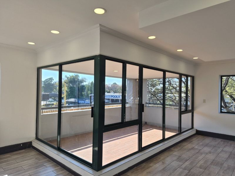 A bright, enclosed balcony area featuring tiled flooring, recessed lighting, and large aluminum-framed glass sliding doors offering an open view.