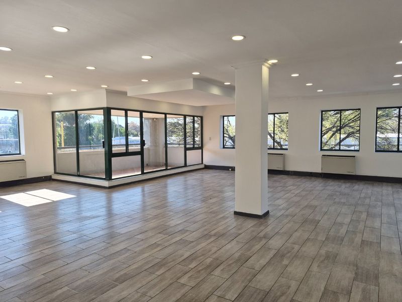 Spacious open-plan commercial office area featuring modern tiled flooring, recessed lighting, large windows, and an integrated enclosed balcony space.