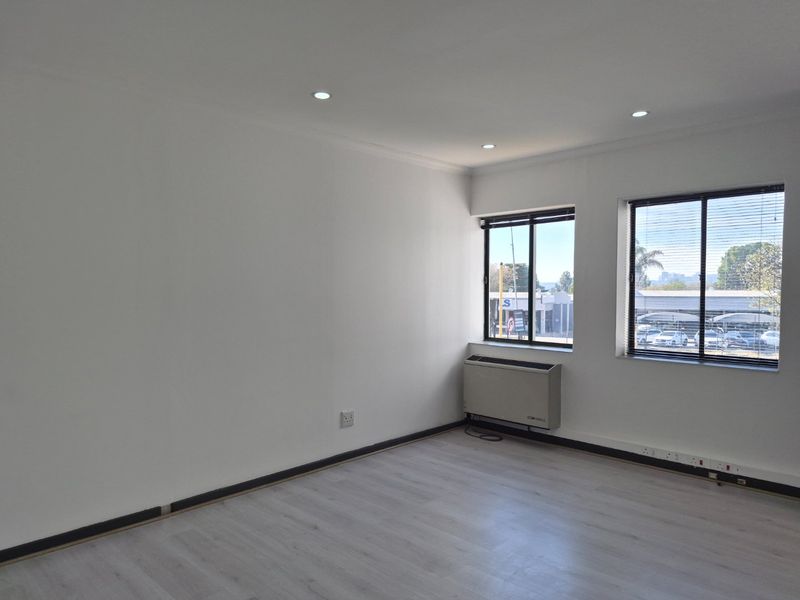 A bright, empty office space featuring laminate flooring, recessed lighting, and an integrated HVAC unit with large windows providing natural light.