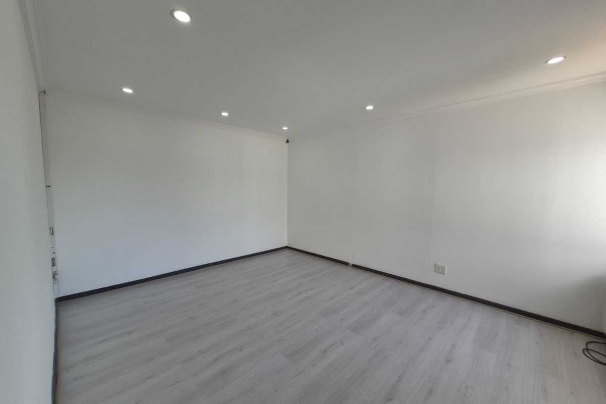A bright, empty living area featuring modern laminate flooring, recessed downlighting, and clean white walls, providing a versatile blank canvas for any commercial use.