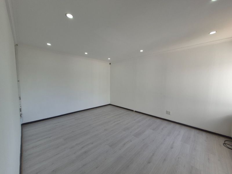 A bright, empty living area featuring modern laminate flooring, recessed downlighting, and clean white walls, providing a versatile blank canvas for any commercial use.