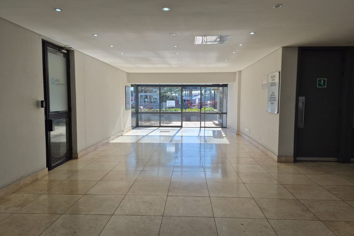 A bright and spacious commercial entrance lobby featuring polished tiled flooring, recessed lighting, and large glass sliding doors leading to the exterior.