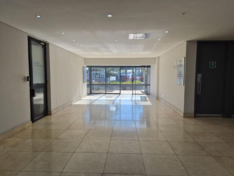 A bright and spacious commercial entrance lobby featuring polished tiled flooring, recessed lighting, and large glass sliding doors leading to the exterior.