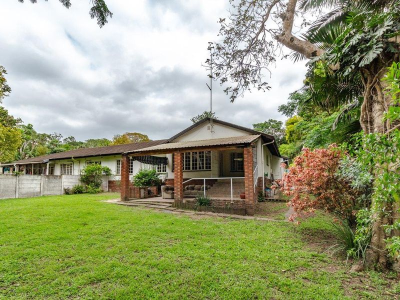 Rear view of the house featuring a covered brick patio, established garden, and concrete boundary wall.