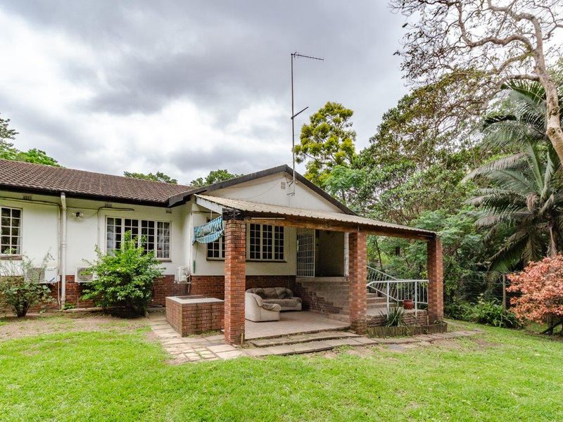 Rear view of the house featuring a covered brick patio, tiled roof, and established garden surroundings.