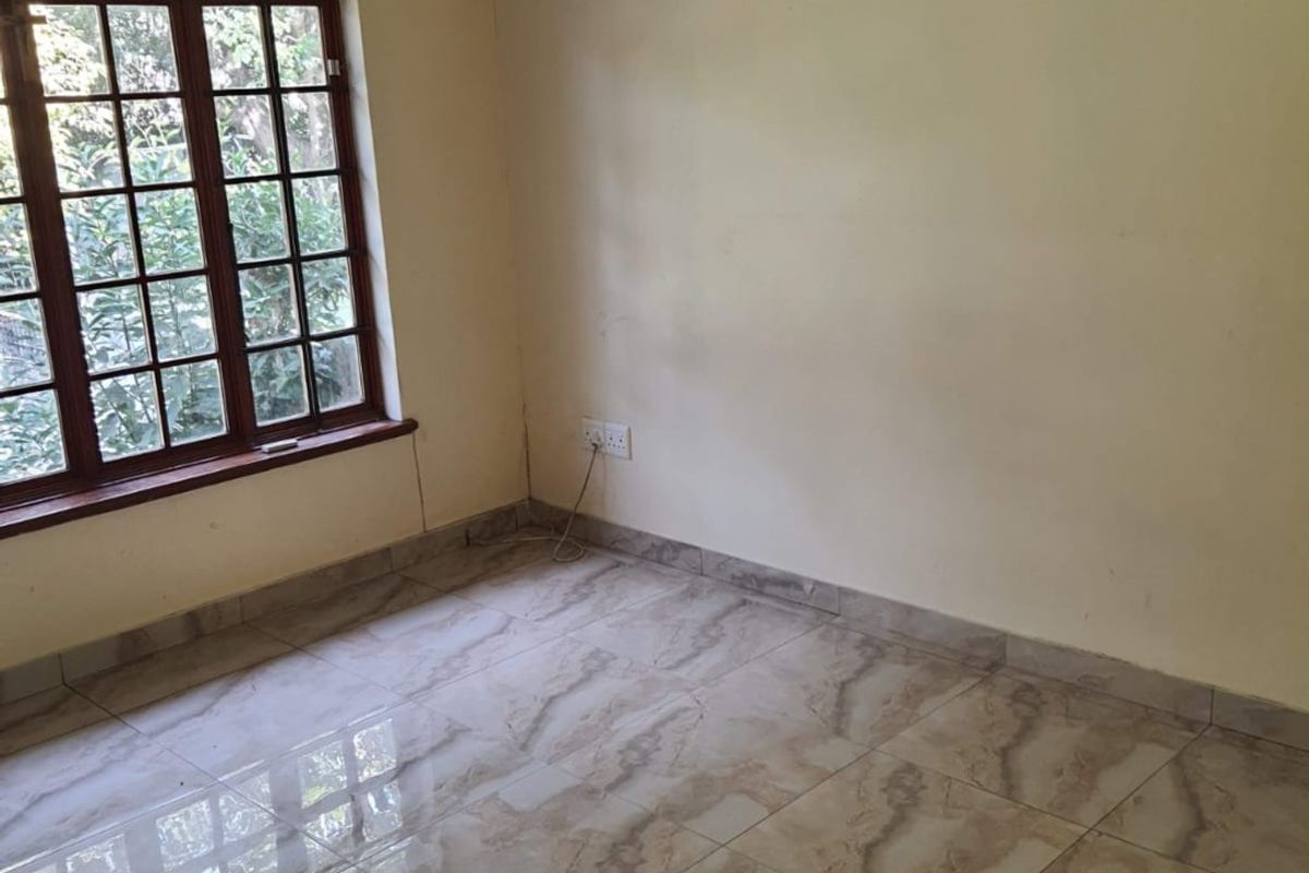 An empty bedroom featuring tiled flooring, a ceiling fan, and a wall-mounted air conditioning unit with wooden window frames.