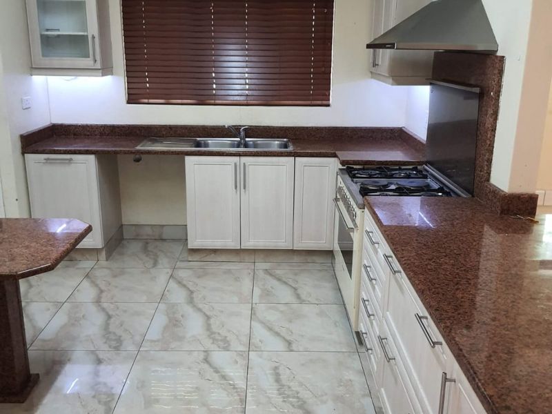 A well-maintained kitchen featuring granite countertops, built-in oven and gas hob, stainless steel extractor fan, and tiled flooring with ample cabinetry.