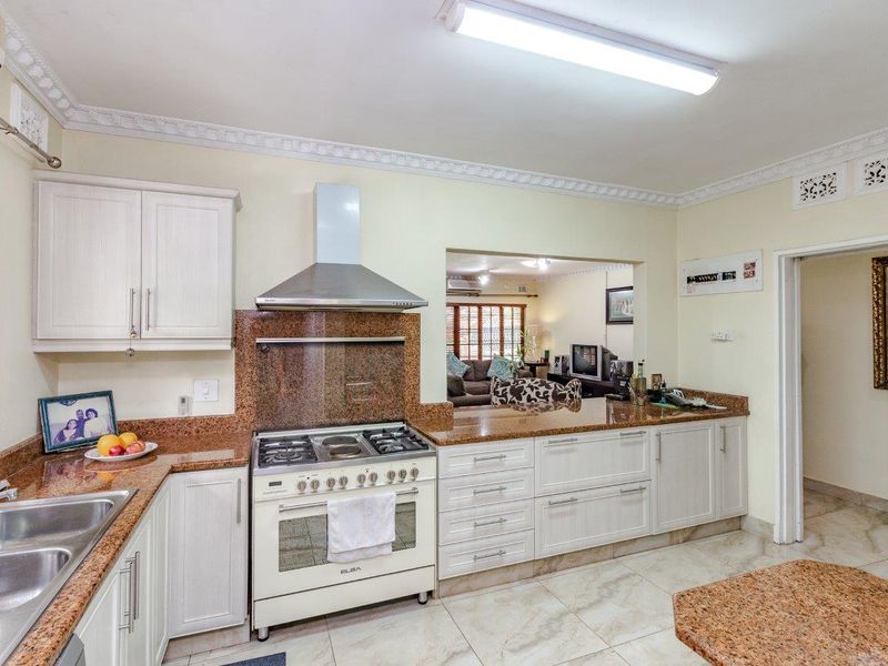 A functional kitchen featuring granite countertops, a gas stove with extractor fan, ample built-in cabinetry, and tiled flooring, with an open pass-through to the living area.