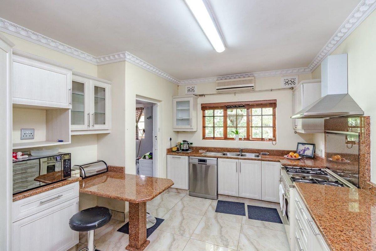 A functional kitchen featuring granite countertops, white cabinetry, a gas hob with extractor fan, and tiled flooring with access to a separate laundry area.