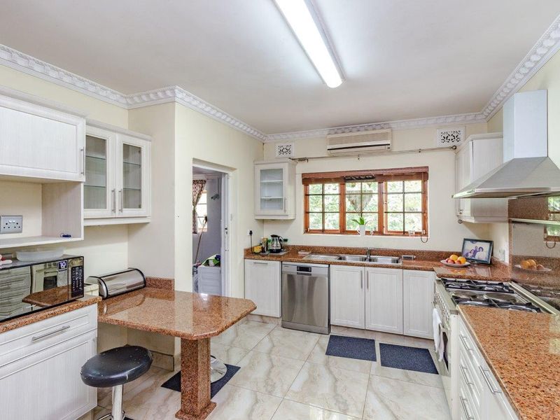 A functional kitchen featuring granite countertops, white cabinetry, a gas hob with extractor fan, and tiled flooring with access to a separate laundry area.