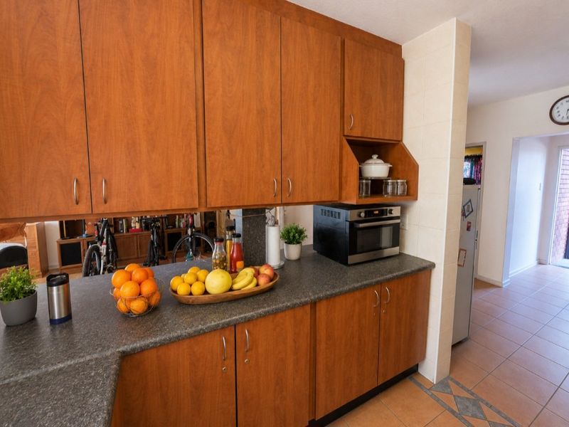 A functional kitchen area featuring wood-tone cabinetry, dark laminate countertops, and tiled flooring, providing a practical workspace with integrated appliance storage.