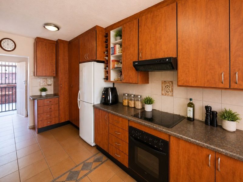 A functional kitchen featuring wood-finish cabinetry, dark laminate countertops, ceramic tile flooring, and integrated cooking appliances, with direct access to an outdoor area.