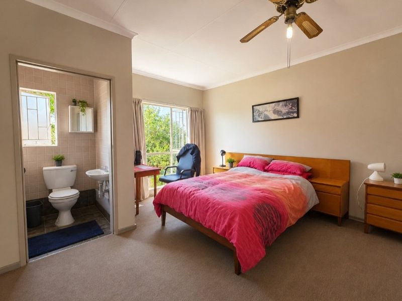 A bedroom featuring a ceiling fan, carpeted flooring, and an attached en-suite bathroom with a toilet and basin.