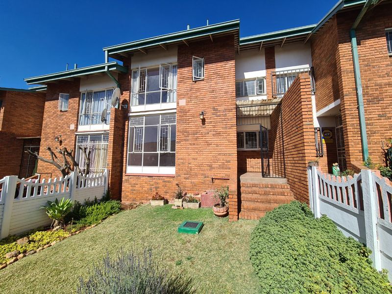 Front elevation of a face brick townhouse featuring a small garden, concrete steps leading to the entrance, and secure metal-framed windows.
