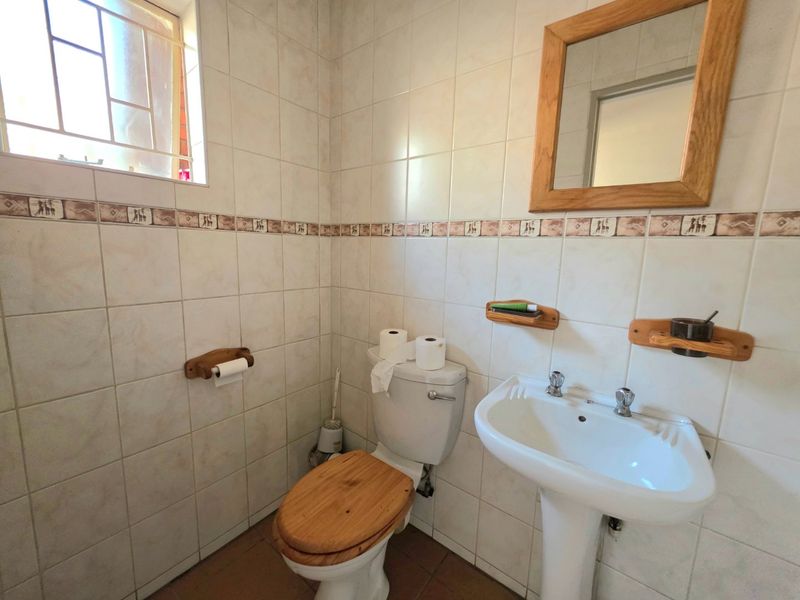 A functional bathroom featuring a pedestal basin, ceramic toilet, and neutral wall tiling with decorative border accents.