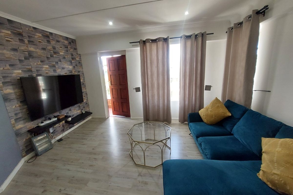 A well-maintained living room featuring modern laminate flooring, a textured feature wall, and recessed lighting, with direct access to an exterior entrance.