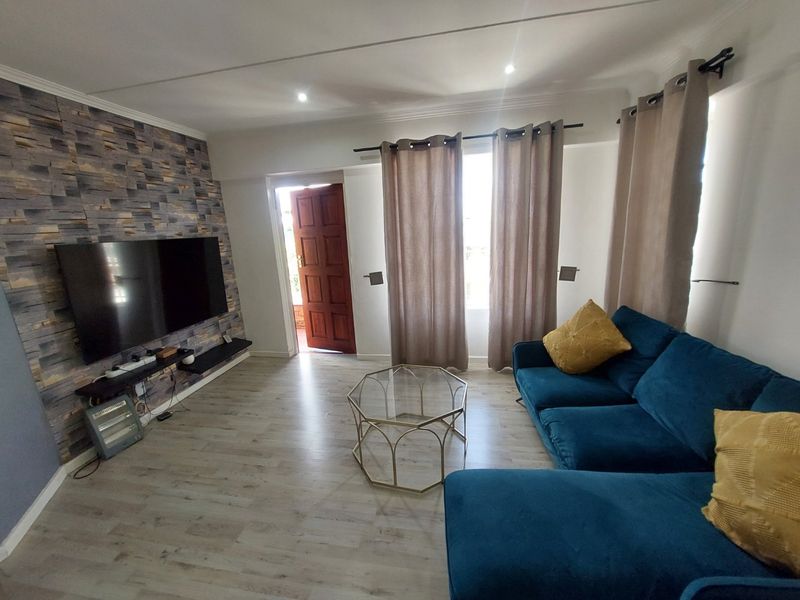 A well-maintained living room featuring modern laminate flooring, a textured feature wall, and recessed lighting, with direct access to an exterior entrance.