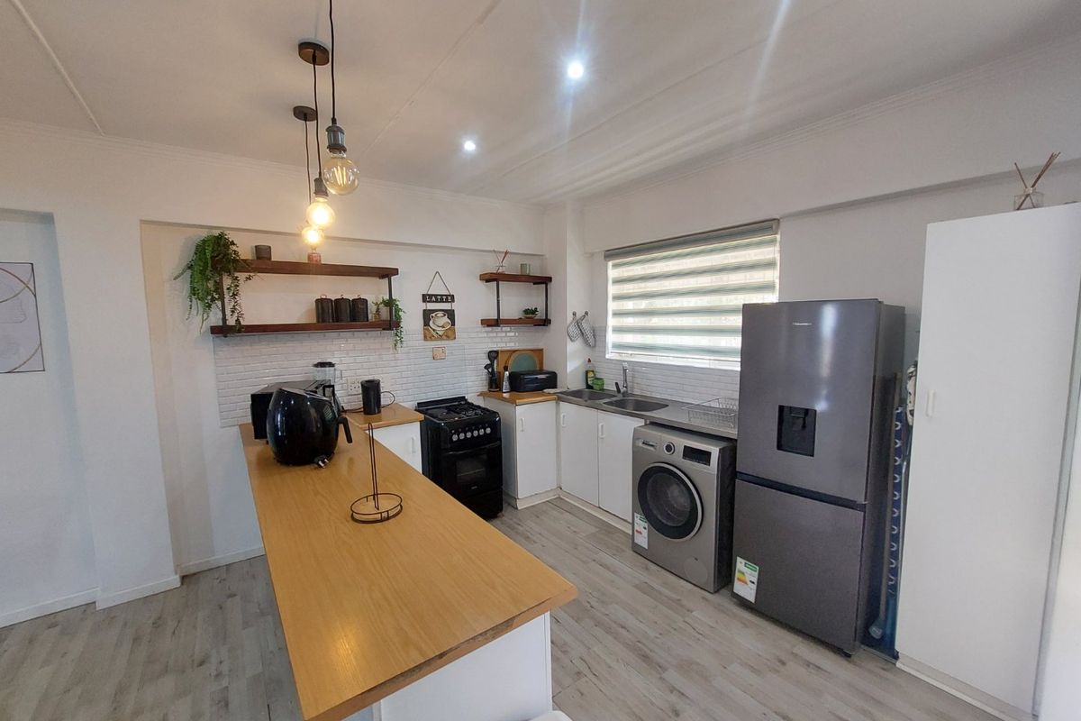 Modern kitchen featuring white cabinetry, subway tile backsplash, timber floating shelves, and a breakfast bar, complemented by contemporary pendant lighting and laminate flooring.