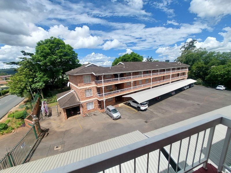 An elevated aerial view of a multi-story brick apartment complex featuring covered parking bays and surrounding landscaped grounds.