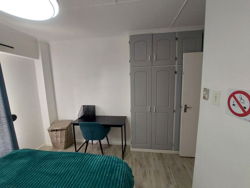 A bedroom featuring light-toned laminate flooring and grey built-in cupboards, providing functional storage space within the room.