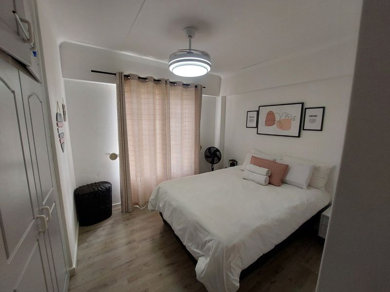 A well-maintained bedroom featuring laminate flooring, built-in cupboards, and a ceiling fan with an integrated light fixture.
