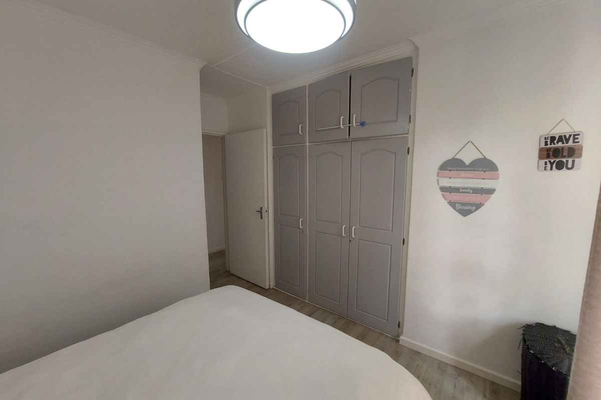 A bedroom featuring built-in grey cupboards, laminate flooring, and a central flush mount ceiling light fixture.