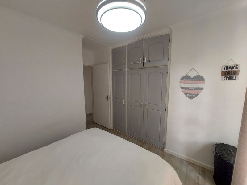 A bedroom featuring built-in grey cupboards, laminate flooring, and a central flush mount ceiling light fixture.