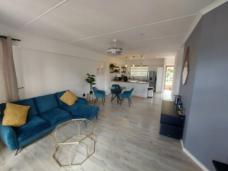 Spacious open-plan living and dining area featuring modern laminate flooring, a functional kitchen island, and contemporary lighting fixtures throughout the space.