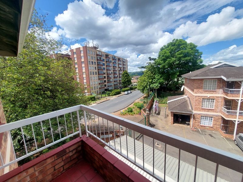 A private balcony featuring a metal balustrade and tiled flooring, offering an elevated view of the surrounding residential complex and street.