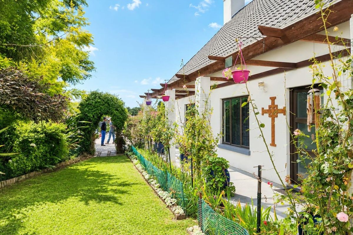 A well-maintained rear exterior view featuring a tiled roof, timber pergola, paved patio area, and a lush landscaped garden with a garden archway.