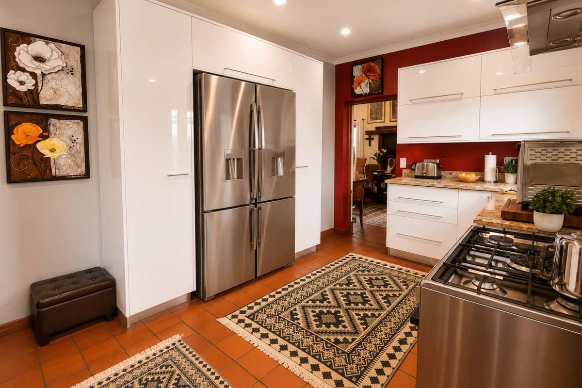 Modern kitchen featuring white high-gloss cabinetry, granite countertops, a stainless steel gas stove, and an extractor fan, with terracotta floor tiles.