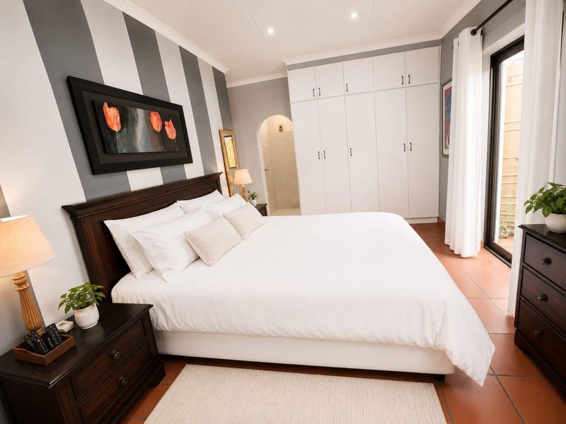 Spacious bedroom featuring built-in cupboards, terracotta tiled flooring, and direct access to an outdoor area through a sliding glass door.