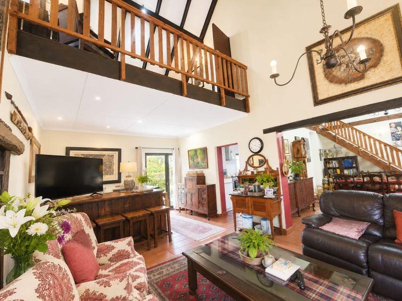Spacious open-plan living area featuring a mezzanine level, exposed timber beams, terracotta flooring, and a built-in bar, creating a warm and character-filled interior space.