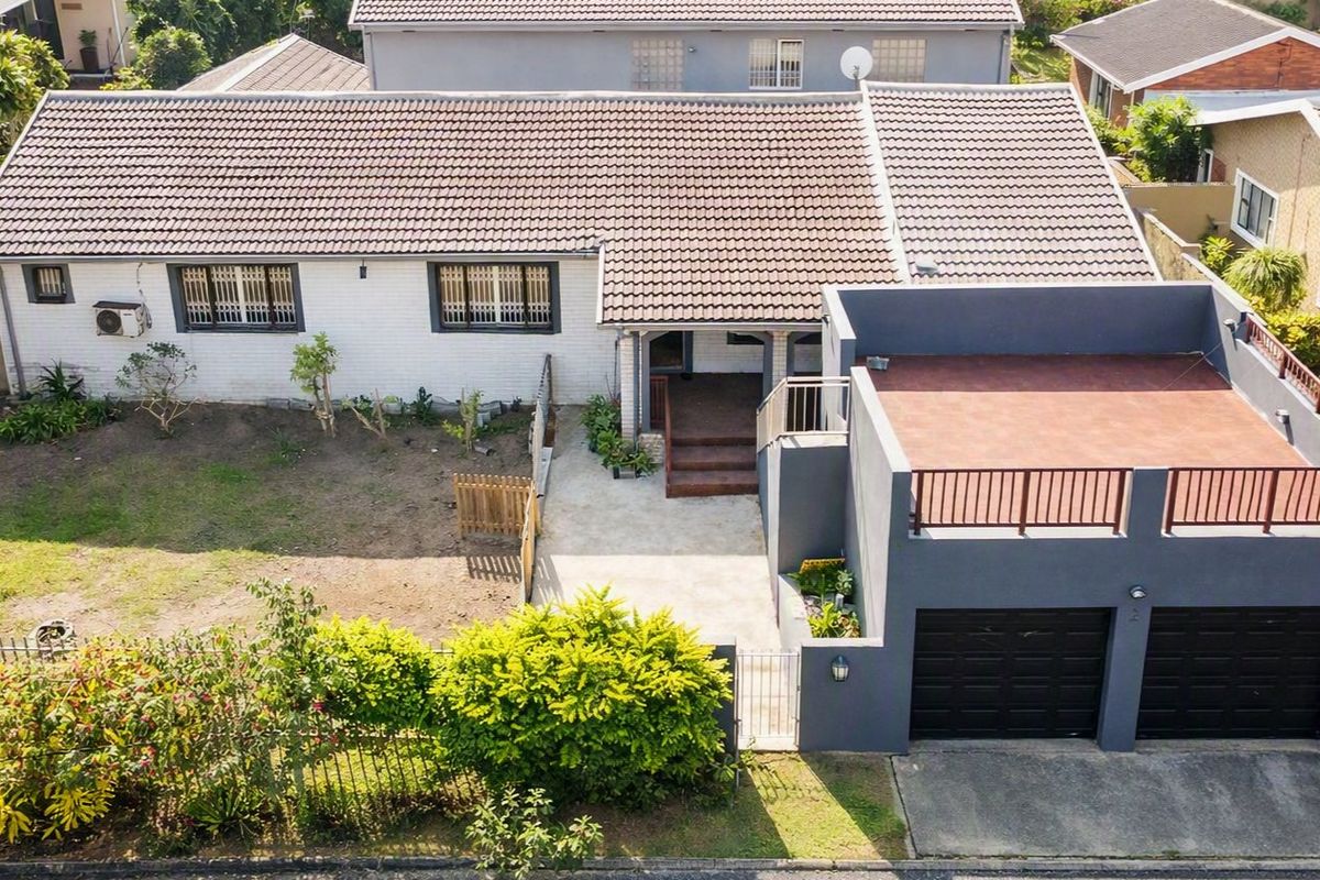 Aerial view of a residential property featuring a tiled roof, double garage with a rooftop terrace, and a front garden area.
