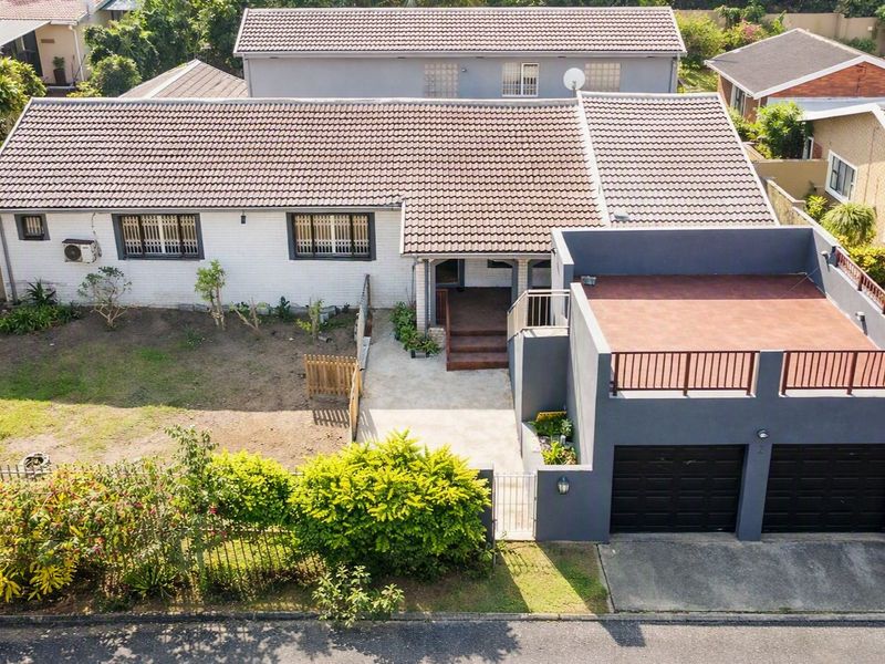 Aerial view of a residential property featuring a tiled roof, double garage with a rooftop terrace, and a front garden area.