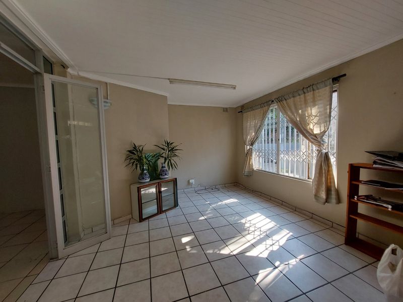 A spacious, empty living area featuring tiled flooring, security gates on windows, and a tongue and groove ceiling, ready for a modern update.