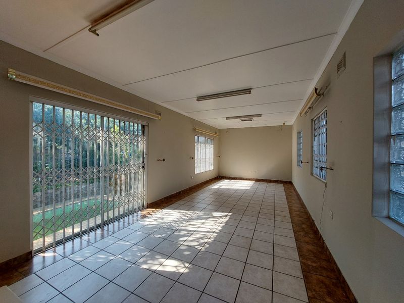 A spacious, empty living area featuring ceramic tile flooring, large sliding glass doors with security gates, and natural light from glass block windows.