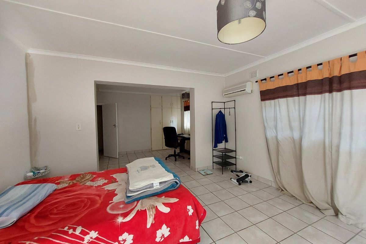 Spacious bedroom featuring tiled flooring, built-in cupboards, and an integrated air conditioning unit, with an adjoining area suitable for a home office.