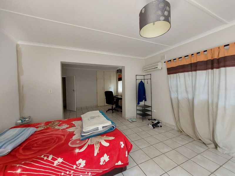 Spacious bedroom featuring tiled flooring, built-in cupboards, and an integrated air conditioning unit, with an adjoining area suitable for a home office.