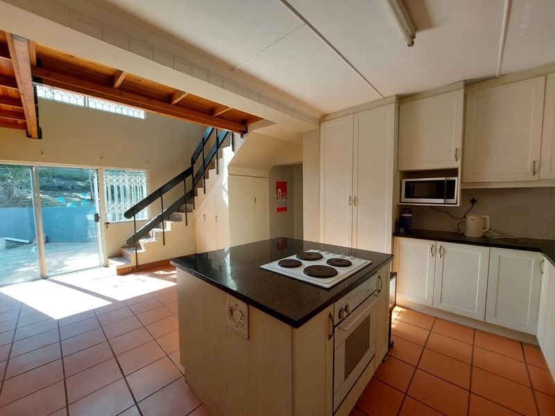 Open plan kitchen and living area featuring a central island with hob, built-in cabinetry, tiled flooring, and a staircase leading to the upper level.