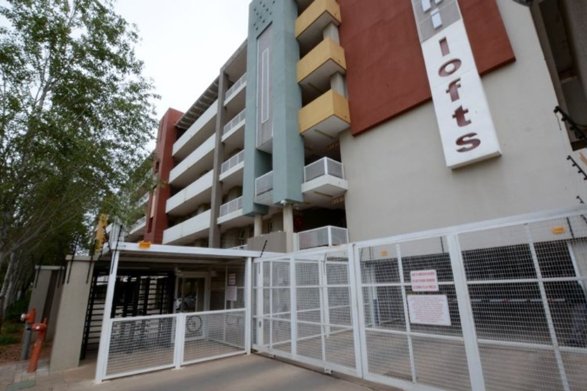Exterior view of the apartment complex entrance featuring secure gated access, multi-level balconies, and prominent building signage.