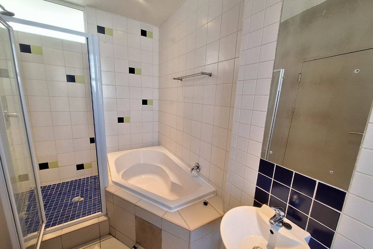 A dated bathroom featuring a separate shower enclosure, built-in bathtub, and pedestal basin, requiring cosmetic updates to the tiling and wall finishes.