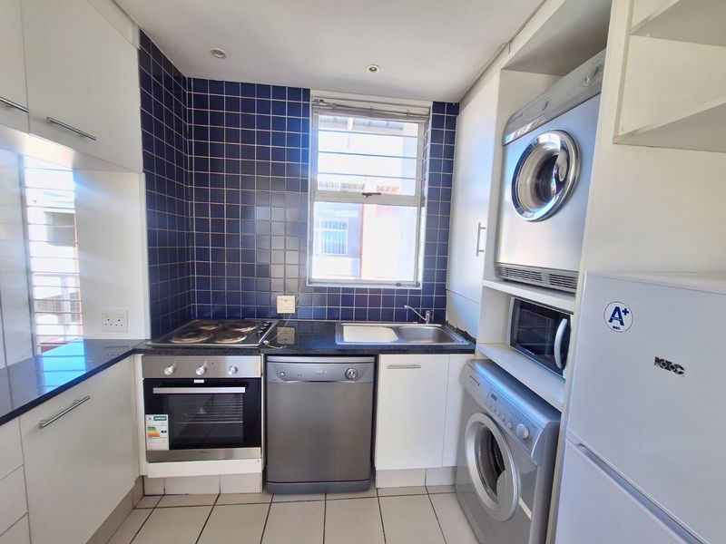 Compact kitchen featuring built-in oven, electric hob, granite countertops, and blue tiled splashback, with integrated space for laundry appliances.